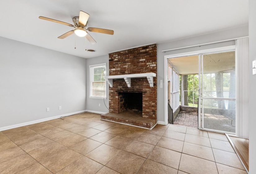 Living area featuring a brick fireplace with a white mantel, tile flooring, a ceiling fan with light fixture, and a sliding glass door opening to a screened porch