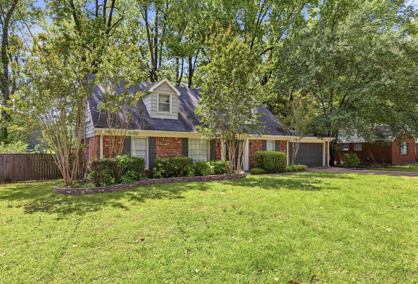 Brick facade home featuring a prominent dormer window, dark shutters, and an attached garage