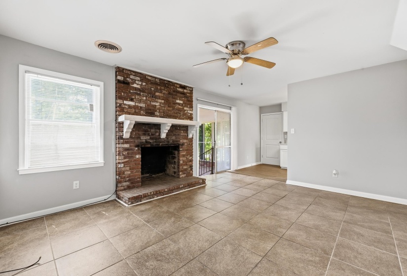Spacious living area featuring a brick-faced fireplace with a white mantel, tile flooring, and a ceiling fan with light fixture