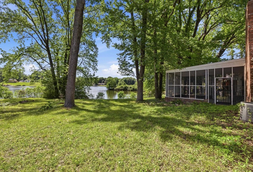 Expansive lawn area featuring mature trees and a screened-in porch with a brick foundation