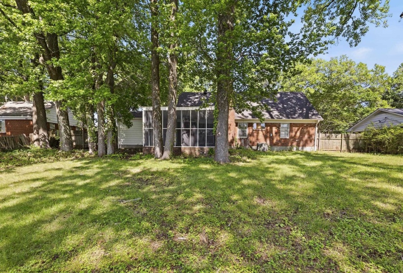 Expansive rear yard featuring a large grassy area, mature trees, a screened porch, and a brick exterior with white siding