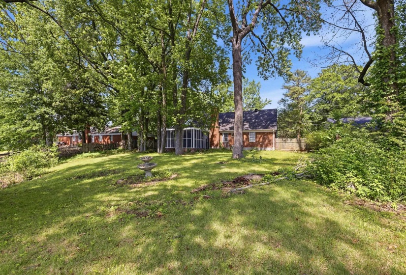 Expansive grassy yard with mature trees and a tiered stone fountain