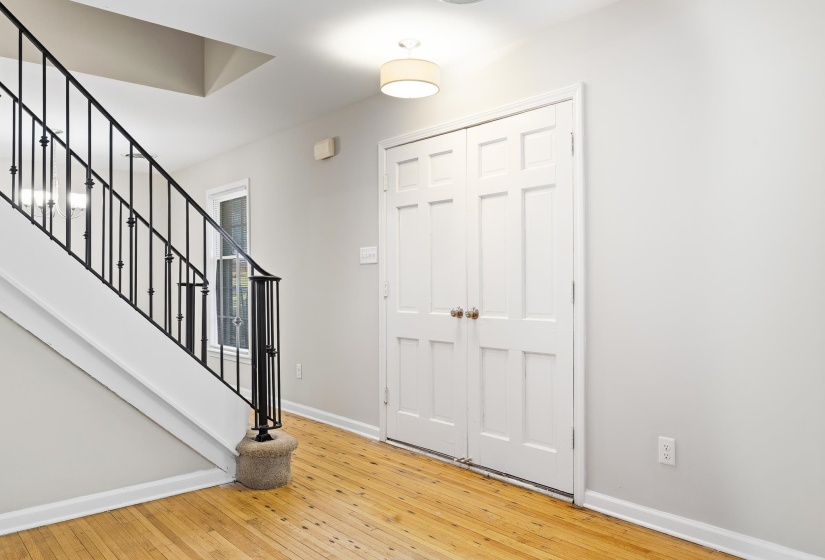 Foyer featuring wood-finish flooring, white paneled doors, and a staircase with black iron railings and white risers