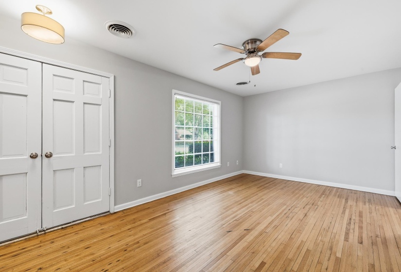 Spacious room featuring wood-finish flooring, a ceiling fan with light, a large multi-pane window, and double panel doors