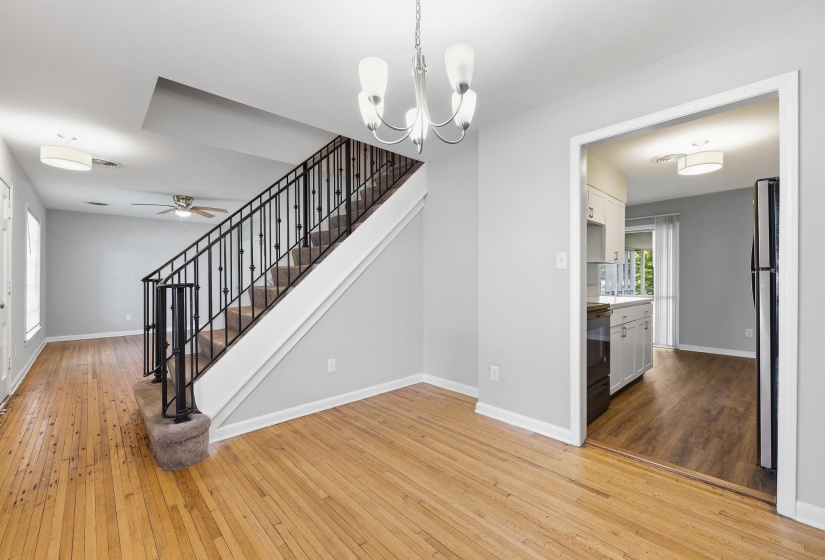 Open living space featuring wood-finish flooring, a contemporary chandelier, and a carpeted staircase with a wrought-iron railing