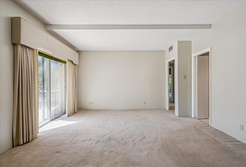 Living area featuring a large sliding glass door, neutral carpeting, light-toned walls, a textured ceiling, and exposed ceiling beams