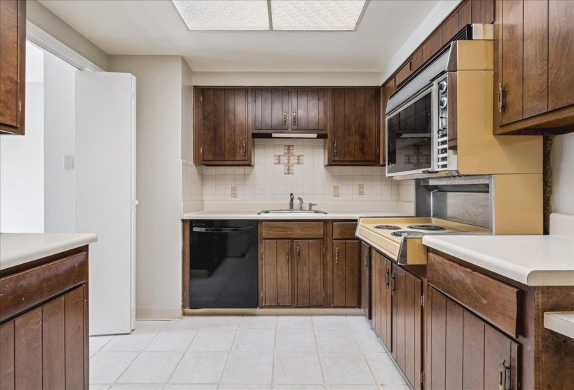 Kitchen featuring wood-panel cabinetry, a built-in microwave, and a white tile floor