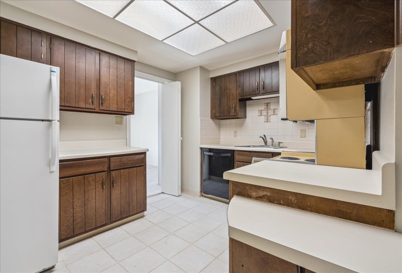 Efficient kitchen layout featuring wood cabinetry, white countertops, tile flooring, and a luminous ceiling panel