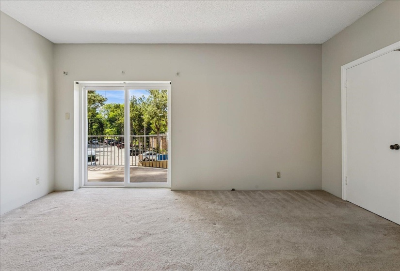 Carpeted interior space featuring a large glass sliding door opening to a balcony with metal railings