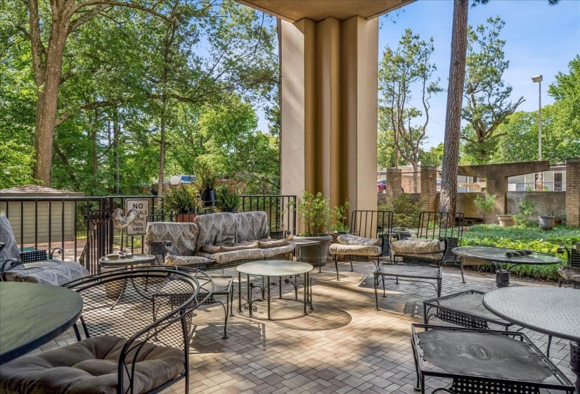 Expansive outdoor patio featuring paver flooring, a black metal railing, and mature surrounding trees