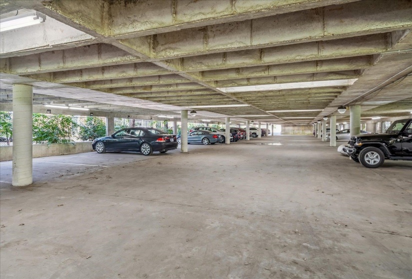Covered parking area featuring concrete flooring, structural columns, and integrated overhead lighting