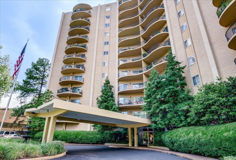 Multi-story residential building featuring a covered entryway, a brick and stucco facade, and multiple curved balconies with glass railings