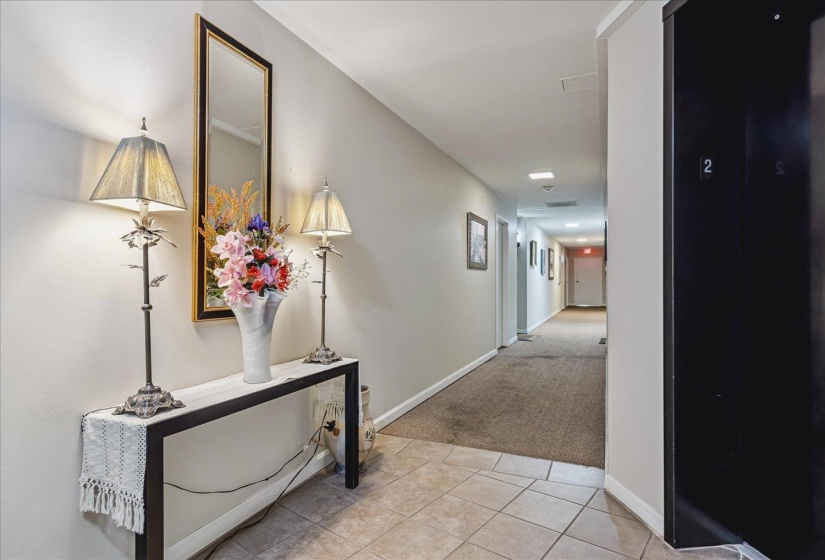 Hallway with light gray walls, recessed lighting, and mixed flooring featuring neutral-toned tile and carpeting