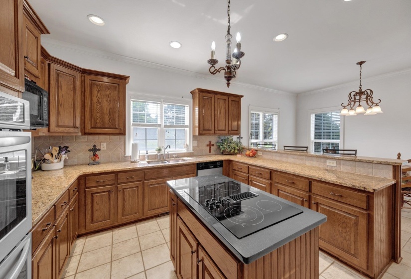 Spacious kitchen featuring warm wood cabinetry, light-toned countertops, and a central island with an integrated cooktop