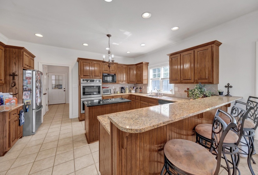 Spacious kitchen featuring warm wood cabinetry, granite countertops, and a large island with an integrated breakfast bar