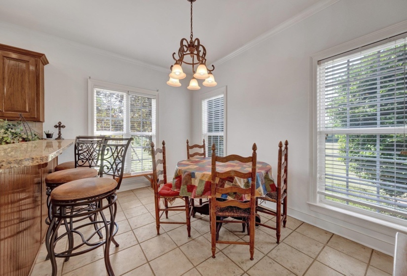 Light-filled dining area featuring tile flooring, crown molding, and a chandelier with frosted glass shades