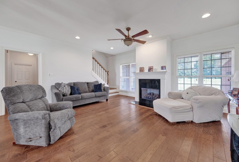 Spacious living area featuring wood-finish flooring, a fireplace with a black surround and white mantel, multiple windows, recessed lighting, and a ceiling fan