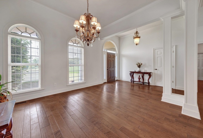 Spacious interior featuring wood-finish flooring, two large arched windows with blinds, a multi-tier chandelier, crown molding, and an arched entry