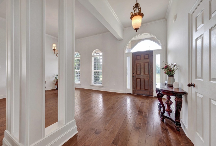 Grand entryway featuring wood-finish flooring, a paneled wood entry door with an arched transom, and fluted architectural columns