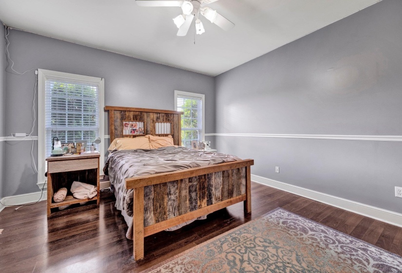 Bedroom featuring wood-finish flooring, light grey walls with white chair rail molding, and a white ceiling fan with integrated lighting