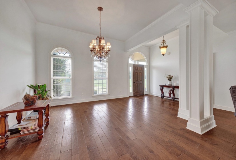 Spacious interior featuring wide-plank wood-finish flooring, a decorative chandelier, and tall arched windows with white blinds