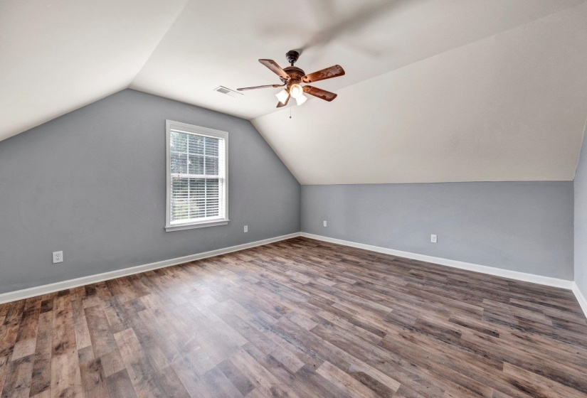 Spacious room featuring wood-finish flooring, a window with blinds, a ceiling fan, and sloped ceilings with painted walls