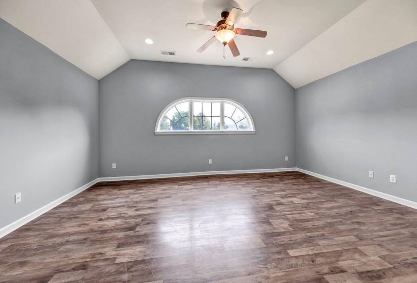 Spacious room featuring vaulted ceilings, a decorative arch-top window, and wood-finish flooring
