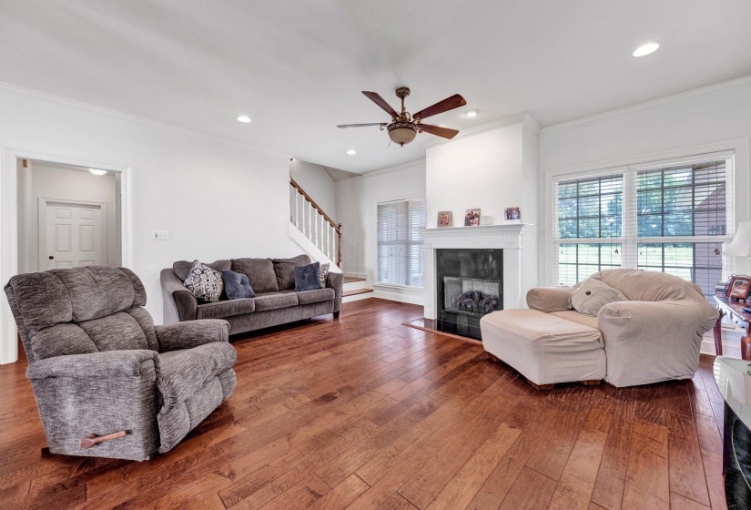 Spacious living area featuring wood-finish flooring, a traditional fireplace with a white mantel, and multiple large windows