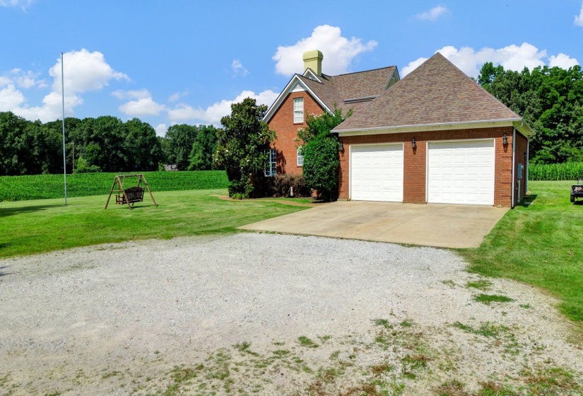 Brick exterior featuring a two-car garage with white paneled doors, concrete driveway, and a gravel parking area