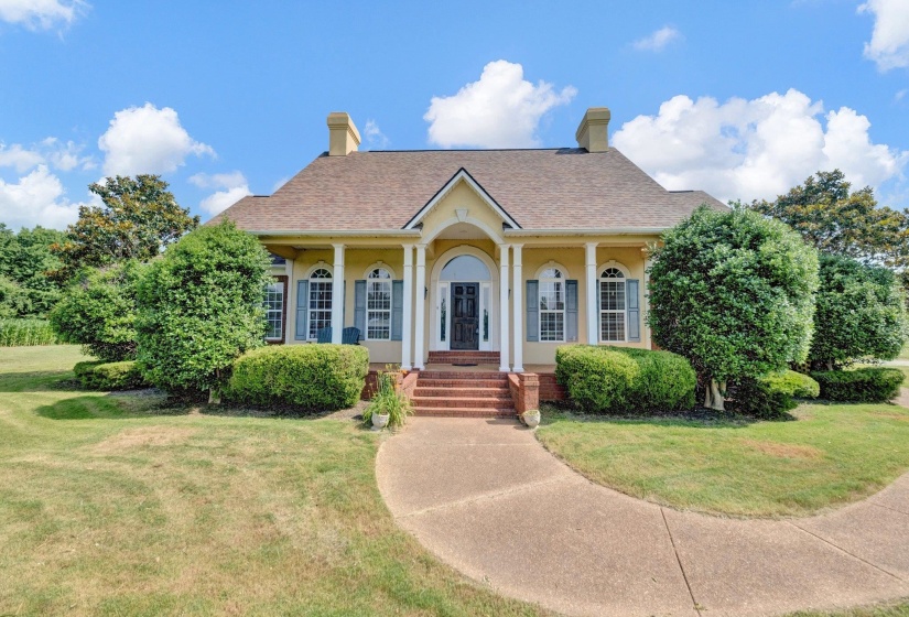 Yellow exterior with a covered porch featuring white columns and brick steps