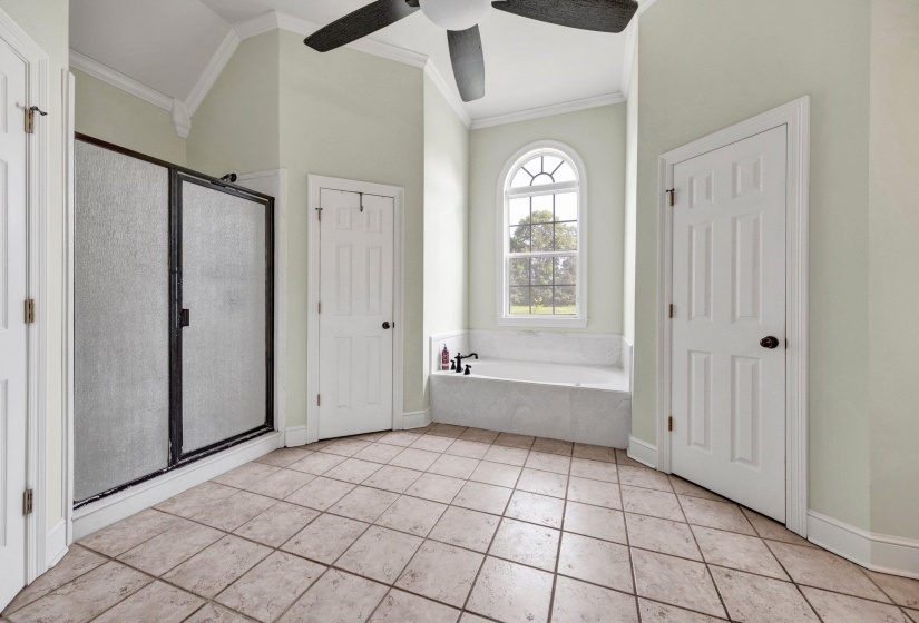 Spacious bathroom featuring diagonal tile flooring, a built-in soaking tub beneath an arched window, a separate shower enclosure, and vaulted ceilings with crown molding