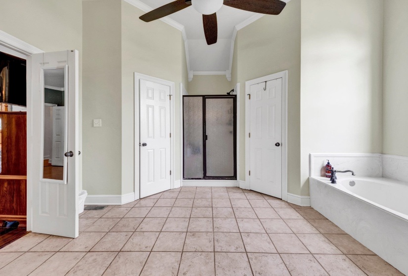 Spacious bathroom featuring light-toned tile flooring, a built-in soaking tub, and a separate shower enclosure with a dark-framed glass door
