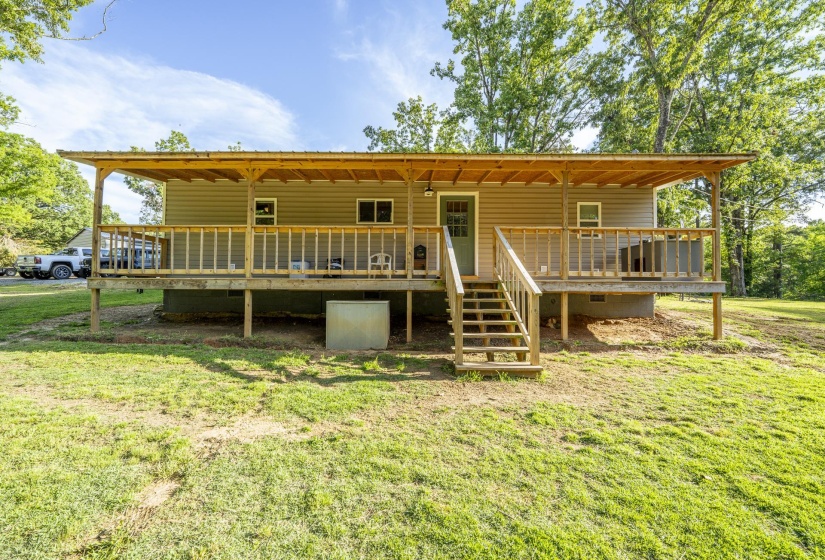 Rear exterior featuring a covered wood-frame deck with railing, stairs, and a metal roof