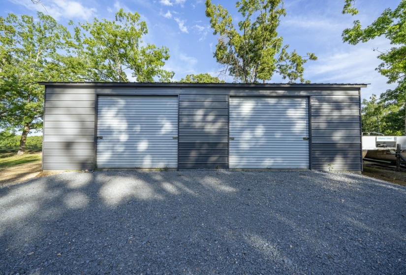 Metal outbuilding with two roll-up doors, a sloped metal roof, and a gravel foreground