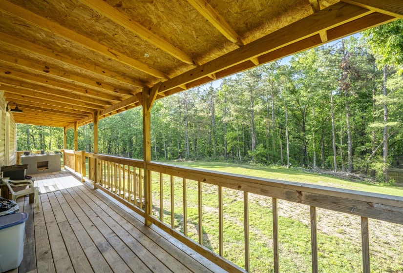 Expansive wooden deck with a covered ceiling, featuring a built-in outdoor kitchen structure and a wooden railing