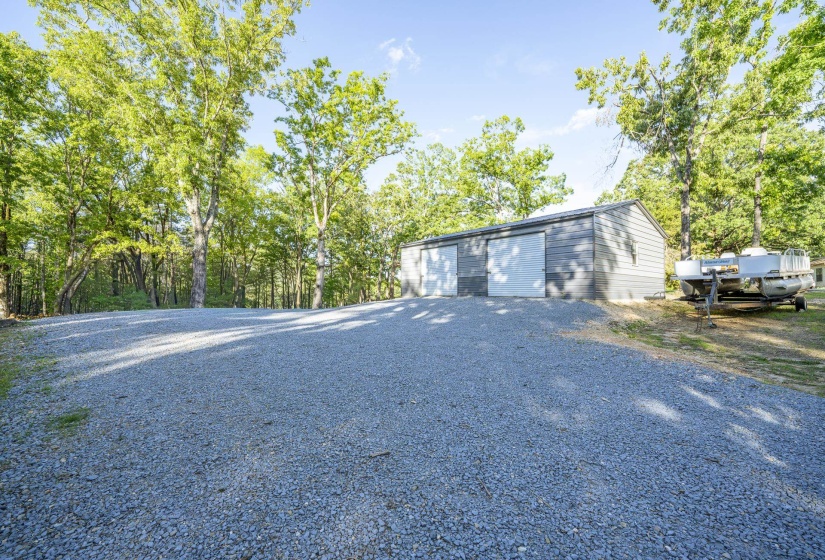Expansive gravel driveway leading to a grey metal storage building with two large garage doors