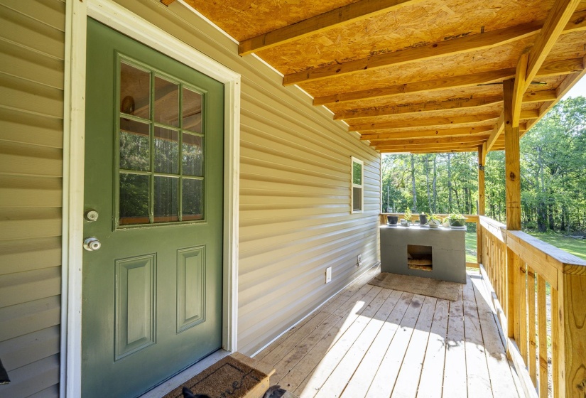 Covered porch with wood-finish flooring, featuring a paneled green door with glass inserts and a built-in outdoor counter