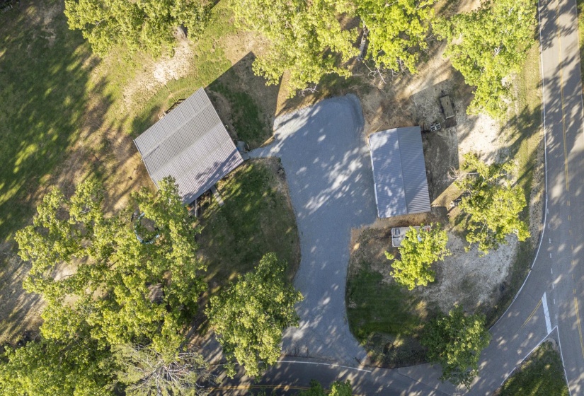 Two detached structures with pitched roofs, surrounded by mature trees and a gravel driveway