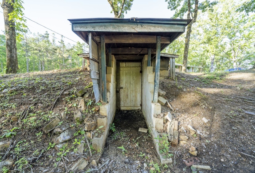 Earthen structure featuring a wooden door, stone and concrete block foundation, and a protective wooden overhang