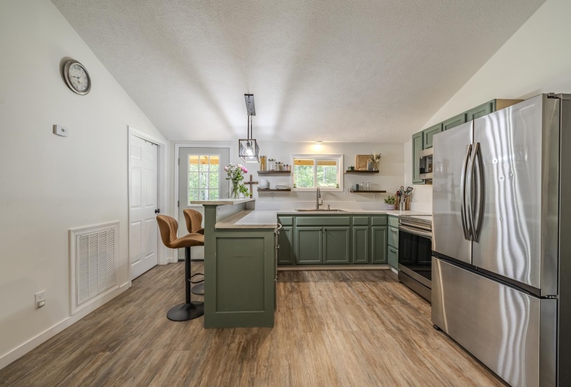 Contemporary kitchen featuring wood-finish flooring, green cabinetry, stainless steel appliances, and a breakfast bar