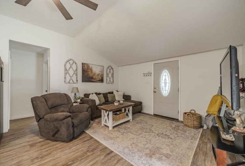 Spacious living area featuring vaulted ceilings, wood-finish flooring, and a white entry door with an oval glass insert