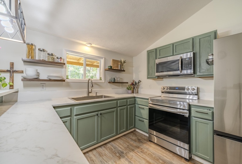 Kitchen featuring light green cabinetry, white countertops, stainless steel appliances, wood-finish flooring, and open shelving