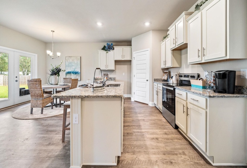 Kitchen featuring a center island with sink, light stone counters, hanging light fixtures, stainless steel electric range oven, and light hardwood / wood-style flooring