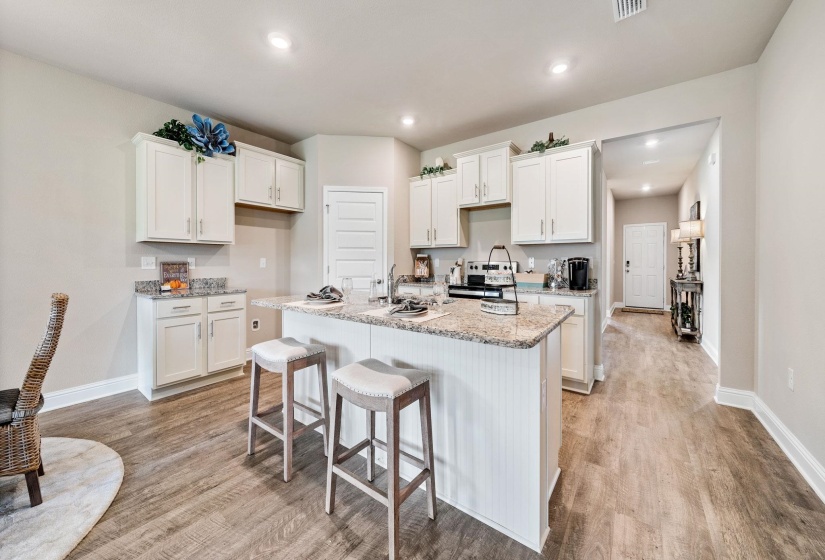 Kitchen with light stone countertops, a center island with sink, and white cabinets