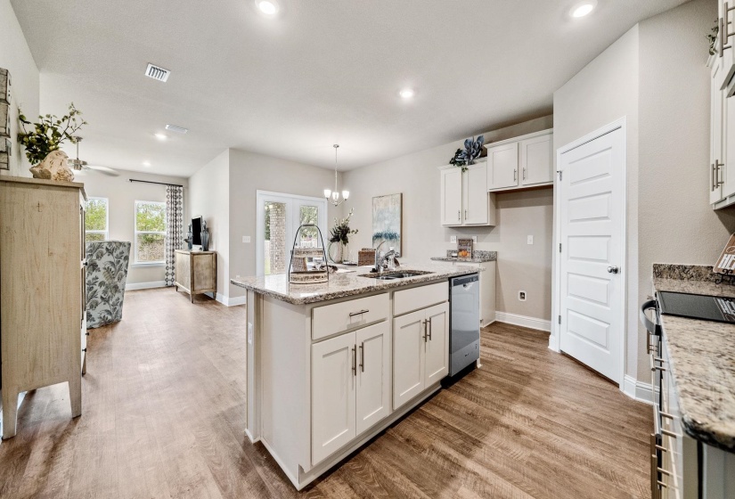 Kitchen with light stone counters, dishwasher, white cabinets, a kitchen island with sink, and pendant lighting