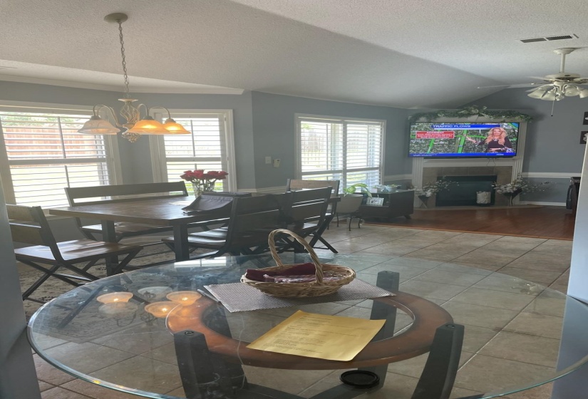 Open-concept living area with vaulted ceilings, a fireplace with a mantel, and plantation shutters