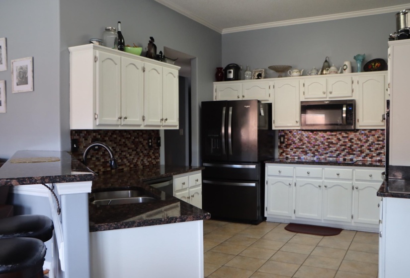 Kitchen with extensive white cabinetry, dark granite-look countertops, and a multi-toned mosaic tile backsplash