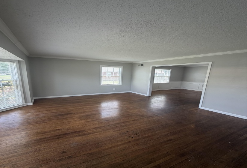Spacious interior room featuring rich wood-finish flooring, light grey painted walls, and white crown molding