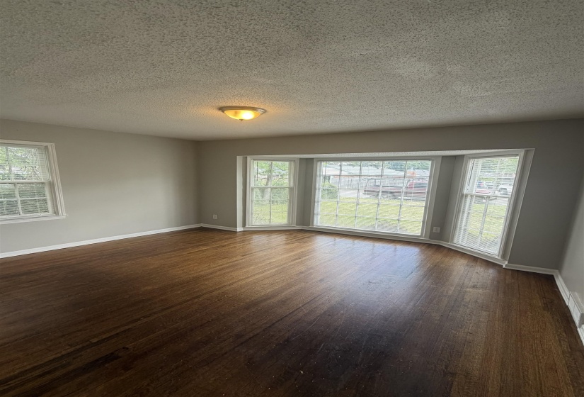 Bay window feature with multiple panes, dark wood-finish flooring, light gray wall paint, white trim, and a semi-flush mount ceiling light