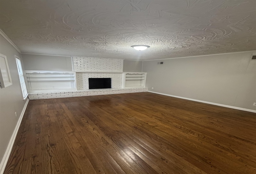 Spacious room featuring wood-finish flooring, a white brick fireplace with a black firebox, integrated shelving units, and a textured ceiling